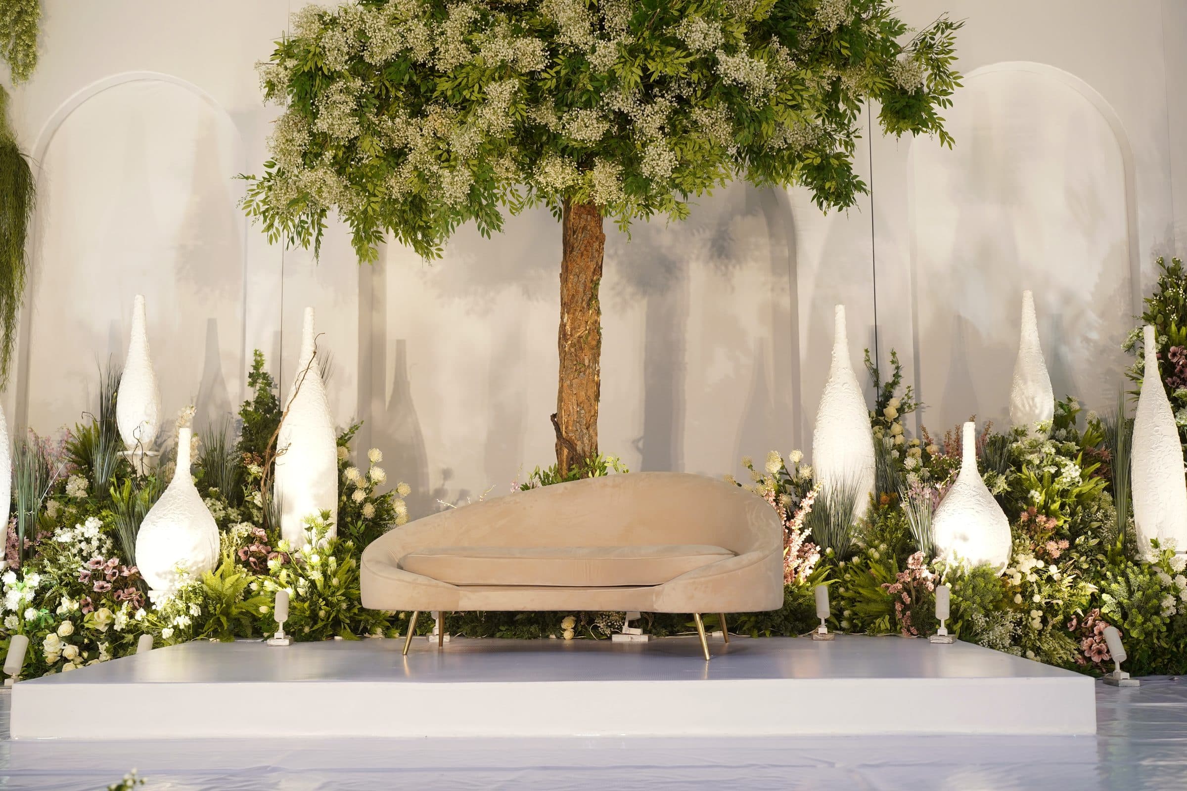 The dressed stage — a tree in blossom above a pale chaise, framed by white florals
